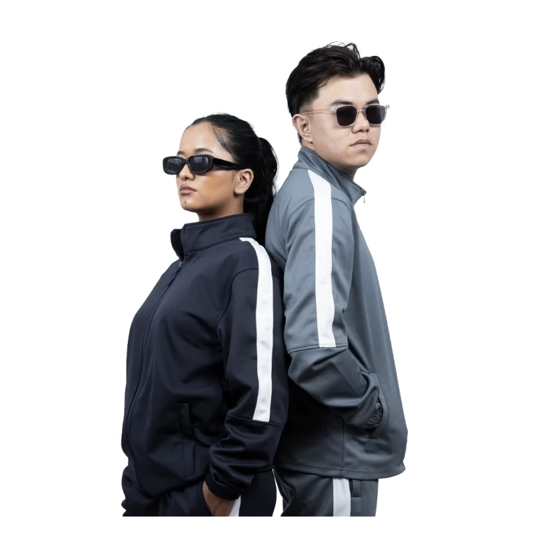 A male and female model standing back-to-back wearing the unisex KTMCTY Strike Track Jacket in grey and navy blue, featuring a classic white stripe down the sleeves
