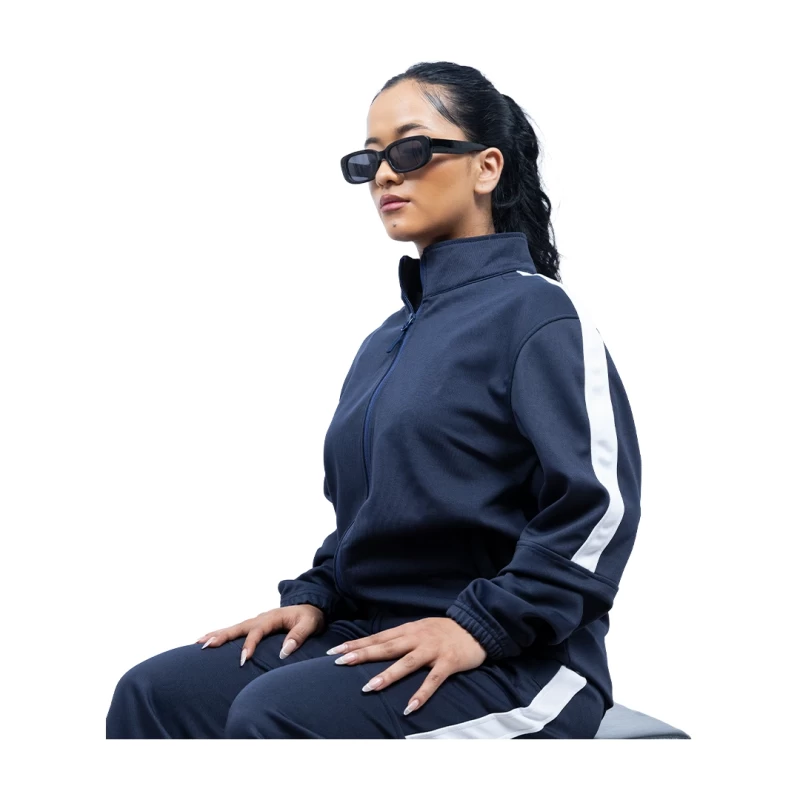 A female and male model standing back-to-back against a white background, wearing matching KTM CTY Strike track jackets with a bold white stripe down the sleeves. The woman is wearing a black track jacket and the man is wearing a grey track jacket. 2