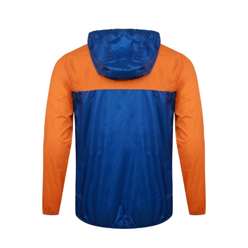 Front view of a male model styling a vibrant red and blue color-block lightweight windcheater jacket. This casual Unisex Windbreaker Jacket features a full zipper and a protective hood, making it a great outer layer for summer wear jacket. 1