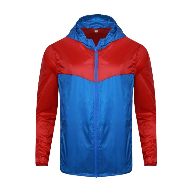Front view of a male model styling a vibrant red and blue color-block lightweight windcheater jacket. This casual Unisex Windbreaker Jacket features a full zipper and a protective hood, making it a great outer layer for summer wear jacket. 1